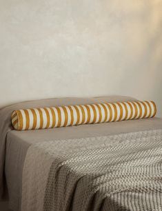 a bed with a striped pillow on top of it next to a white wall and lamp