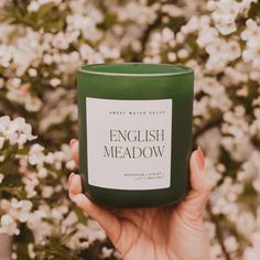 a hand holding a green candle in front of some white and pink flowers with the words english meadow written on it