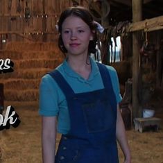 a woman standing in front of a pile of hay with the caption, there is an image of a woman wearing overalls