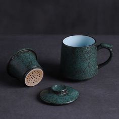 a tea cup with a strainer next to it on a black surface and the lid is open