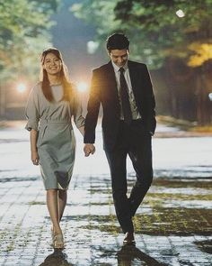 a man and woman are walking down the street at night, one is holding his hand