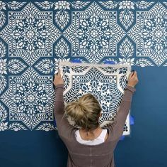 a woman is painting a wall with blue and white stencil designs on it