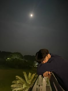 a man leaning his head on a railing looking out at the night sky and moon