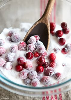 cranberries and powdered sugar in a glass bowl with a wooden spoon on the side