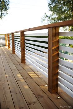 a wooden deck with white railing and wood slats on the sides, along with trees in the background