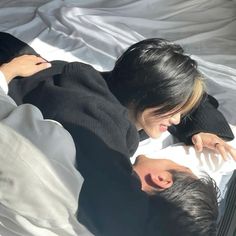 a man and woman laying on top of a bed next to each other in the sunlight