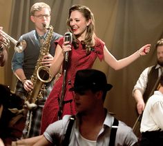 a woman in a red dress is singing into a microphone while two men are playing instruments behind her