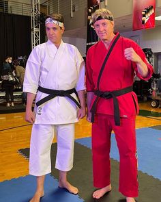 two men standing next to each other on a blue and black mat in a gym