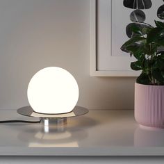 a white light sitting on top of a table next to a potted plant