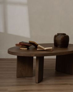 a table with a book and vase on it in front of a wall, next to a wooden floor