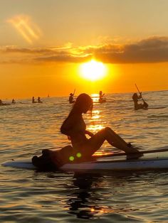 a woman sitting on top of a surfboard in the middle of the ocean at sunset