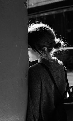 black and white photograph of a woman leaning against a wall with her back to the camera