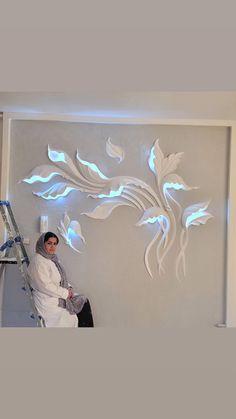 a woman standing on a ladder in front of a wall with flowers and leaves painted on it