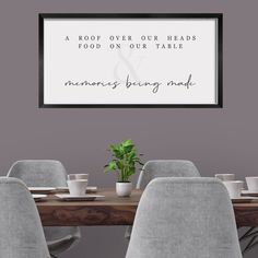 a dining room table with gray chairs and a framed sign above it