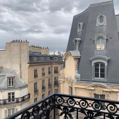 a balcony with an iron railing and building in the background, looking down at buildings