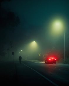 a car driving down a foggy road at night with street lights in the background