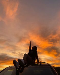 a woman sitting on top of a car in the sunset