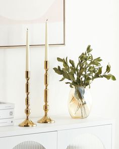 two candles are sitting on top of a white cabinet next to a potted plant