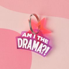 an i am the drama keychain hanging on a pink and purple background with a star