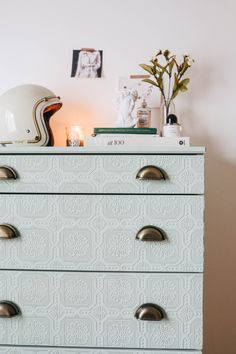 a white chest of drawers with a helmet on top and flowers in the corner next to it