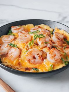 a skillet filled with shrimp and cheese on top of a white counter next to chopsticks