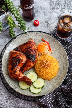 a white plate topped with chicken, rice and cucumber next to a drink