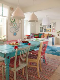 the dining room table is painted in blue and has pink chairs, with colorful rugs on