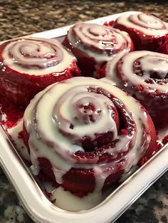 red velvet rolls with white icing in a baking dish on a granite countertop