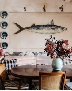 a fish painting on the wall above a table with chairs and flowers in front of it