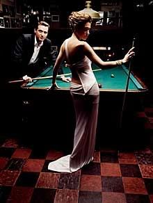 a woman standing next to a pool table with a man in suit and tie behind her