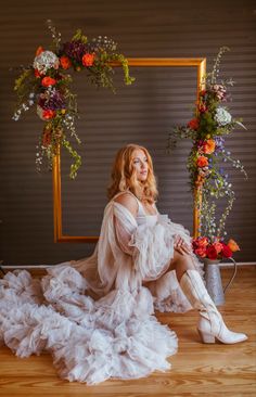 a woman sitting on the floor in front of a mirror with flowers around her legs