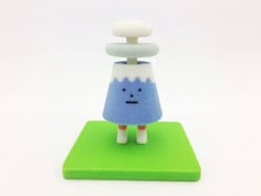 a small blue and white toy with a mushroom on it's head sitting on a green base