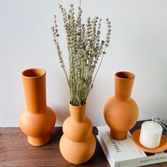 three orange vases sitting on top of a wooden table next to a white candle