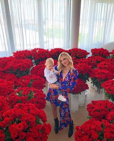 a woman holding a baby in front of red flowers