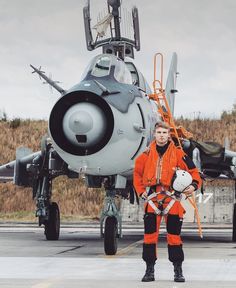 a man in an orange jacket standing next to a fighter jet