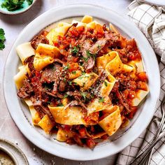 a white bowl filled with pasta and meat on top of a table next to silverware