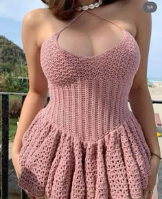 a woman is wearing a pink crochet dress and has her hands in her pockets