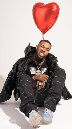 a man sitting on the ground with a red heart balloon attached to his head,