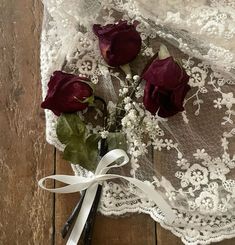 three red roses sitting on top of a lace covered table cloth next to scissors and flowers