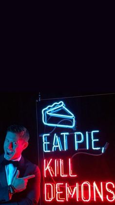 a man standing next to a neon sign that says eat pie, kill demonss