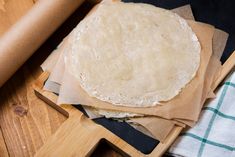 an uncooked tortilla sitting on top of a cutting board next to a rolling pin