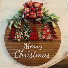 a merry christmas sign hanging on the side of a building with plaid bows and evergreens