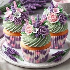 three cupcakes decorated with flowers and purple icing on a plate next to lavender plants