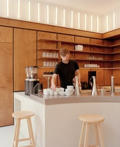 a man standing at a counter preparing food in a kitchen next to two stools