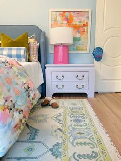 a bed room with a neatly made bed next to a white dresser and a painting on the wall