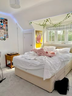 an unmade bed sitting in a bedroom next to a desk and window with pictures on the wall