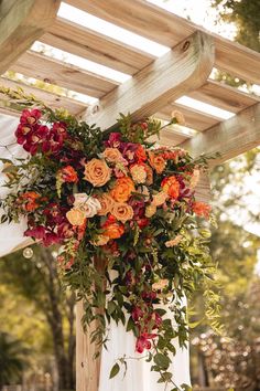 an outdoor wedding ceremony with flowers and greenery hanging from the ceiling over the aisle