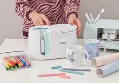 a woman is making crayons on the table next to her coffee mugs