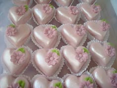 there are many pink heart shaped cakes in the plastic container on the table and one is decorated with flowers