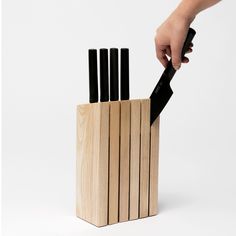 a person holding a knife in a wooden block with four knives sticking out of it